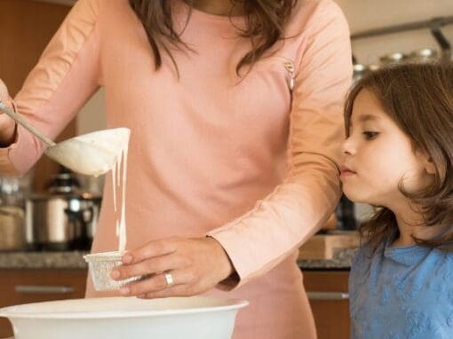 Childminder with a child making some cakes in a home kitchen.