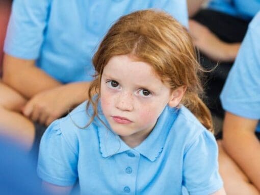 Girl in a school classroom looking serious looking straight at the camera.