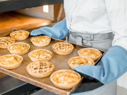 Person holding a tray of pies in a bakery processing plant.