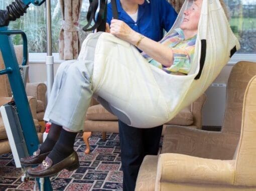 A lady being moved in a sling hoist by her carer.